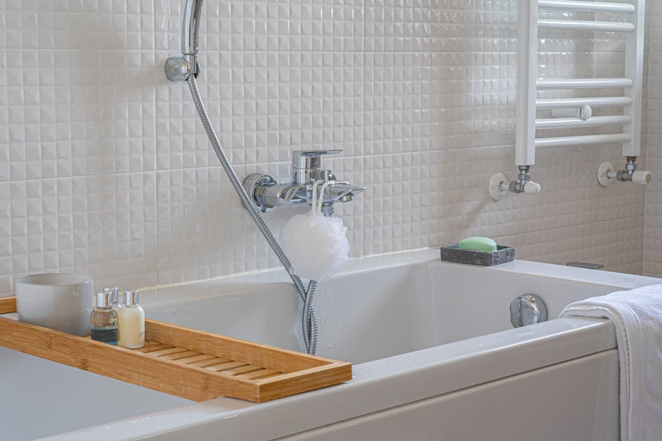 Close-up view of a white bathroom sink with a modern chrome faucet, accompanied by two clear glass soap dispensers filled with white liquid soap and lotion, positioned on the sink's surface. The surface appears clean and shiny, reflecting light, with a clean mirror behind the sink and tiled wall in the background, indicating a well-maintained domestic space. The arrangement exemplifies surface cleaning and hygiene practices, consistent with professional domestic cleaning services by Hounslow Cleaners for end of tenancy and general bathroom upkeep.